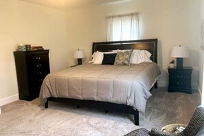 A bedroom with a bed, two bedside tables with lamps, a dresser, and a window with curtains.