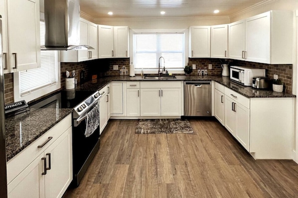 A modern kitchen with white cabinets, granite countertops, a stainless steel range hood, and a dishwasher.