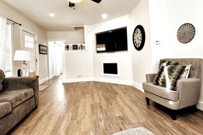 A living room with a fireplace, a clock, and a television mounted on the wall.