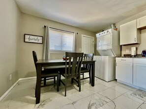 Un comedor con mesa y sillas, una cocina equipada y un ventanal con persianas.