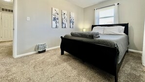 Ein Schlafzimmer mit Bett, einem kleinen Mülleimer, einer Tür und einem Fenster mit Jalousien.