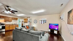 Ein Wohnzimmer mit grauem Sofa, einem Fernseher und einer Küche im Hintergrund.