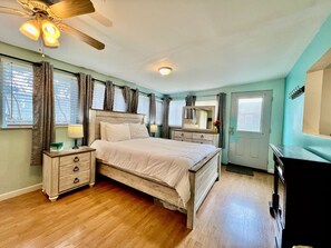 Un dormitorio con cama, mesitas de noche, ventilador de techo y cómoda.