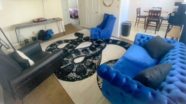 Een woonkamer met een blauwe bank, een kamerkleed met patroon, een flatscreen-tv en een eethoek met stoelen en een tafel.