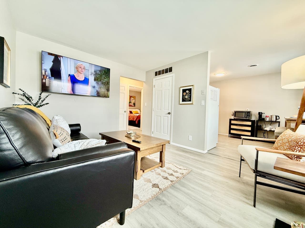 A modern living room with a black leather sofa, a wooden coffee table, and a TV mounted on the wall.