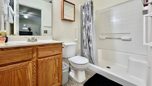 Ein Badezimmer mit einem Holzkonsolenunterschrank, einer weißen Toilette, einer Dusche mit gestreifter Duschvorhang und einem Spiegel über dem Unterschrank.