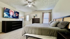 Ein Schlafzimmer mit einem Bett, einem Fernseher, einem Deckenventilator, einer Kommode und einem Fenster.