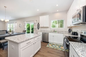 A modern kitchen with a central island, white cabinetry, a built-in oven, and a window with blinds. - NEW  Cheerful 5 bedroom home in quiet suburban area. (Maineville)