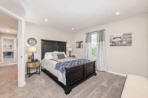 A bedroom with a large bed, bedside tables, a nightstand, a window with curtains, and a wall clock.