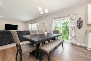 A dining area with a dark wooden table, cushioned chairs, a bench, a potted plant, a wall clock, and a 'Welcome to My Kitchen' sign. - NEW  Cheerful 5 bedroom home in quiet suburban area. (Maineville)