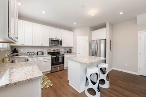 A modern kitchen with white cabinets, stainless steel appliances, and a central island with bar stools.