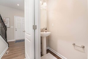 A hallway with a white door, a white sink, and a handrail on the wall.