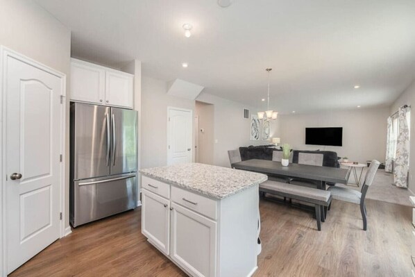 A modern kitchen with white cabinetry, a stainless steel refrigerator, and a dining area with a bench and table.