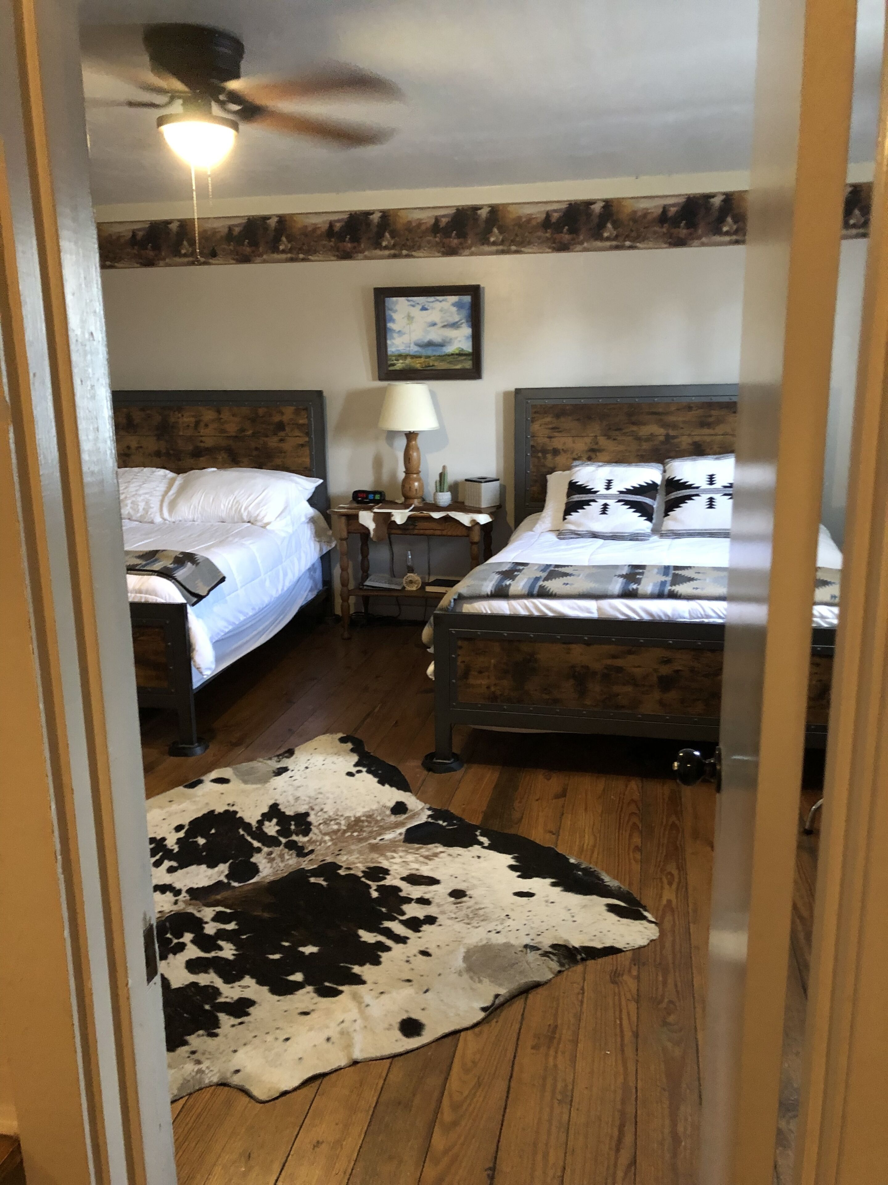 Une chambre avec deux lits, un ventilateur de plafond, une table de chevet avec une lampe et un tapis en peau de vache.