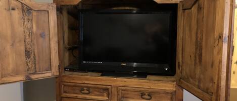A wooden entertainment center with a flat-screen TV, built-in drawers, and a shelf.