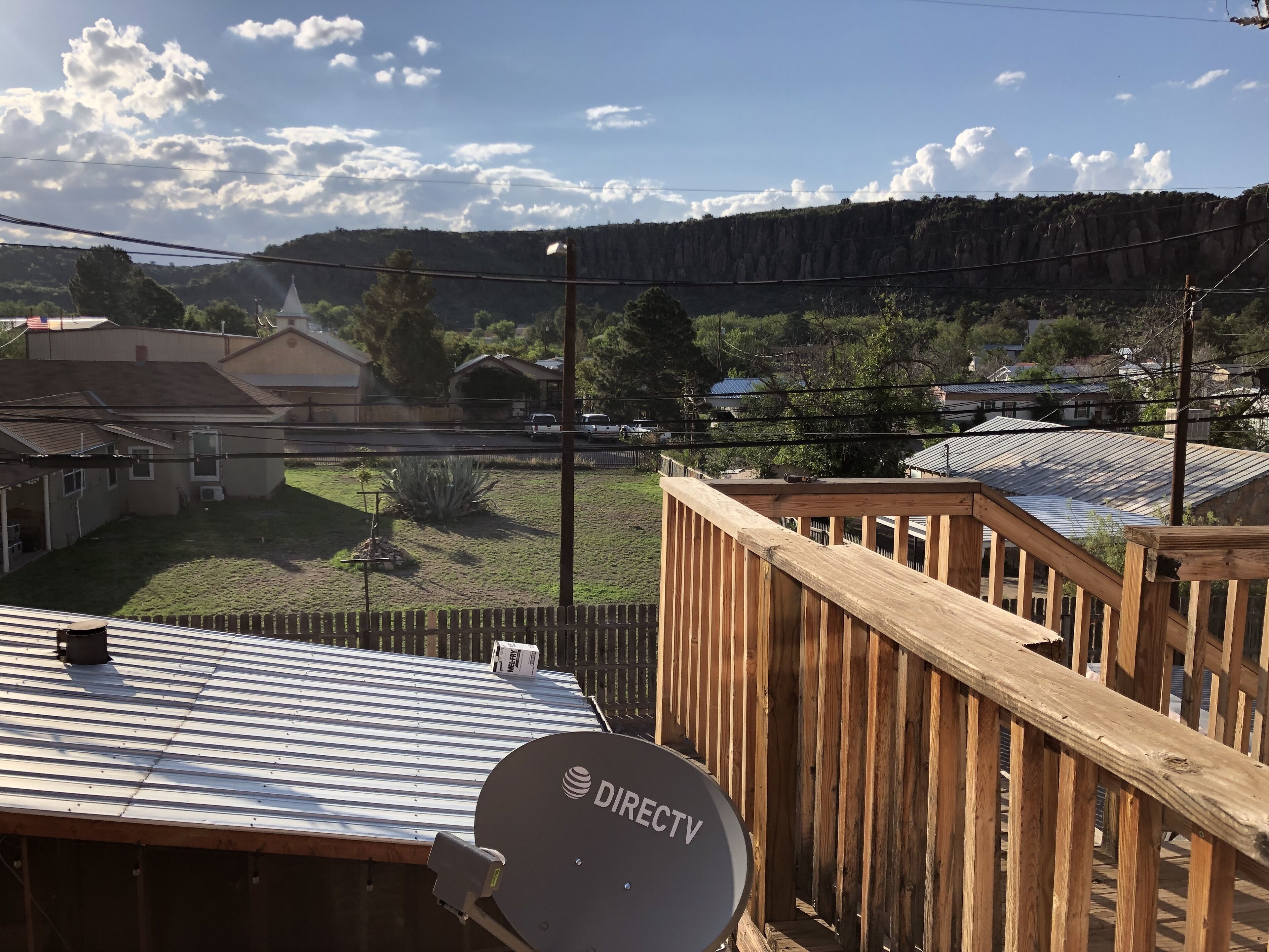 A satellite dish labeled DIRECTV on a metal roof, wooden deck, and a view of a residential area with houses and a mountain in the background.