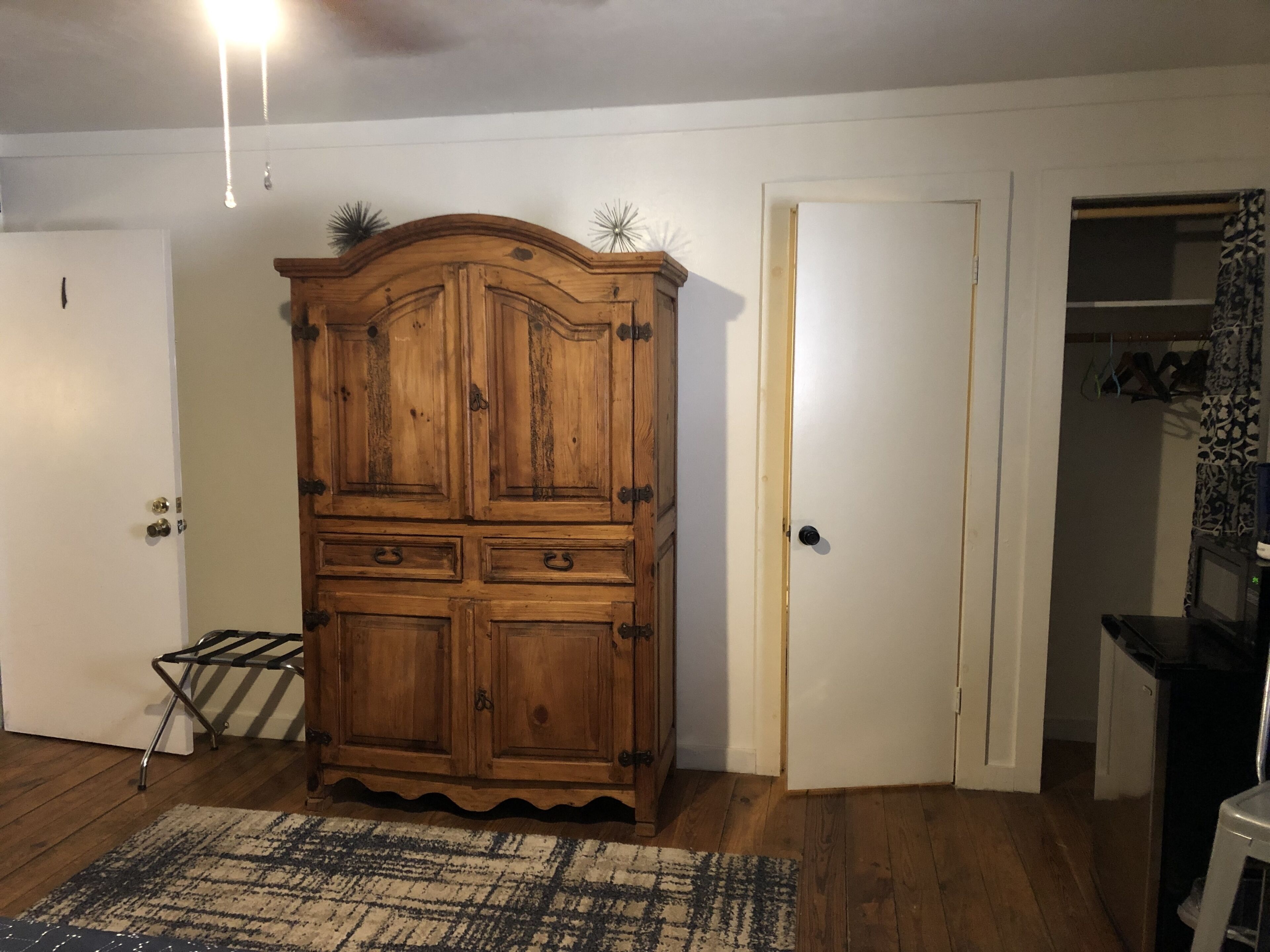Una habitación con un armario de madera, una puerta, una mesita y una alfombra estampada.