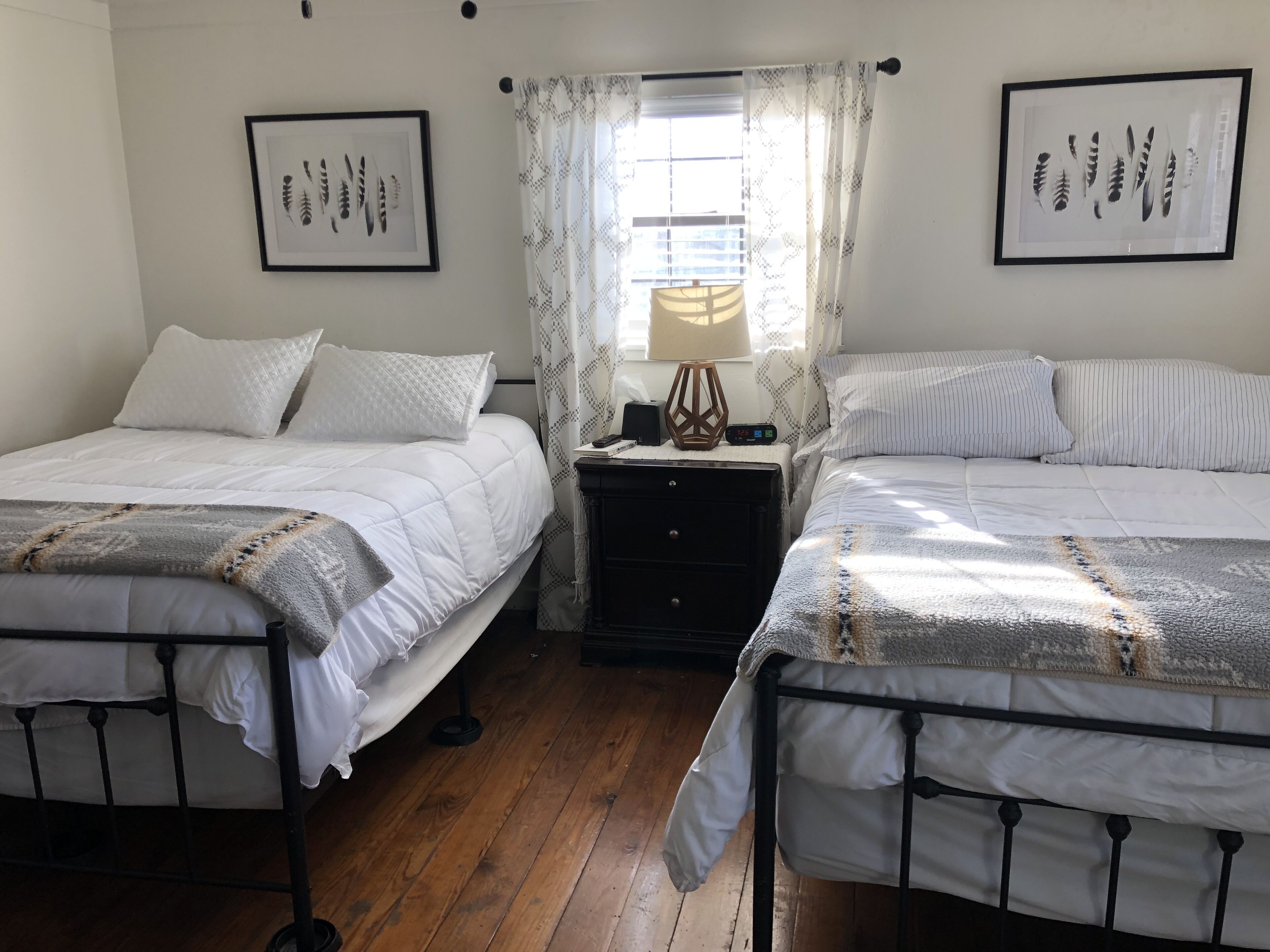 A room with two beds, a nightstand with a lamp, and framed botanical prints on the walls.