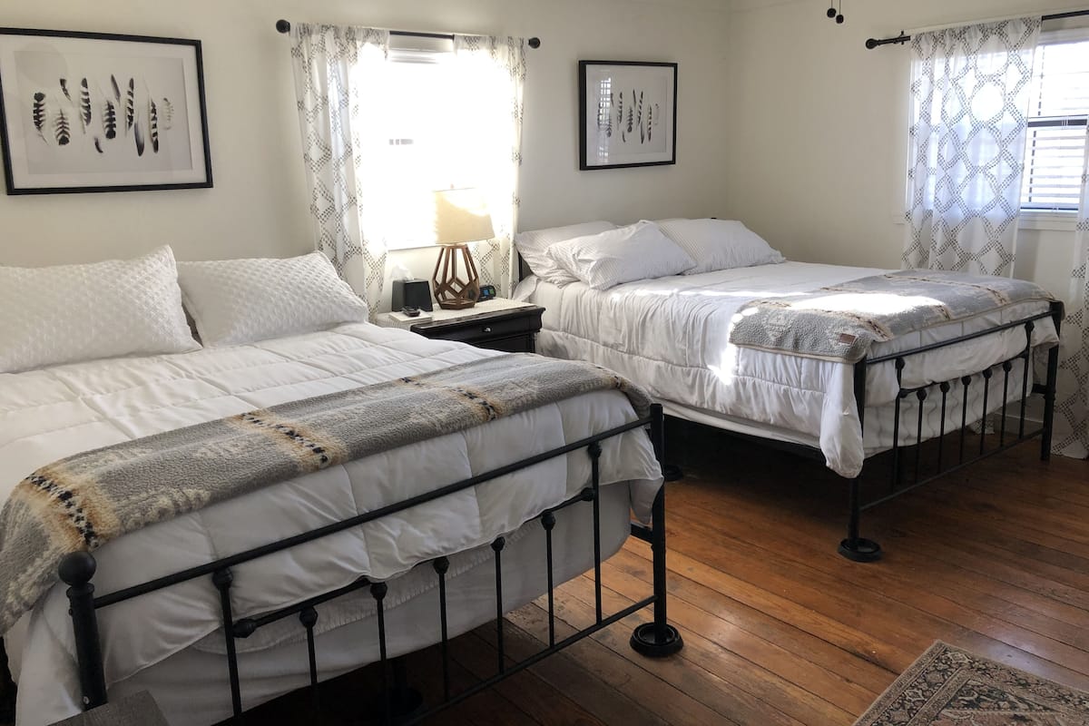 A bedroom with two beds, a nightstand, a lamp, and framed artwork on the wall.