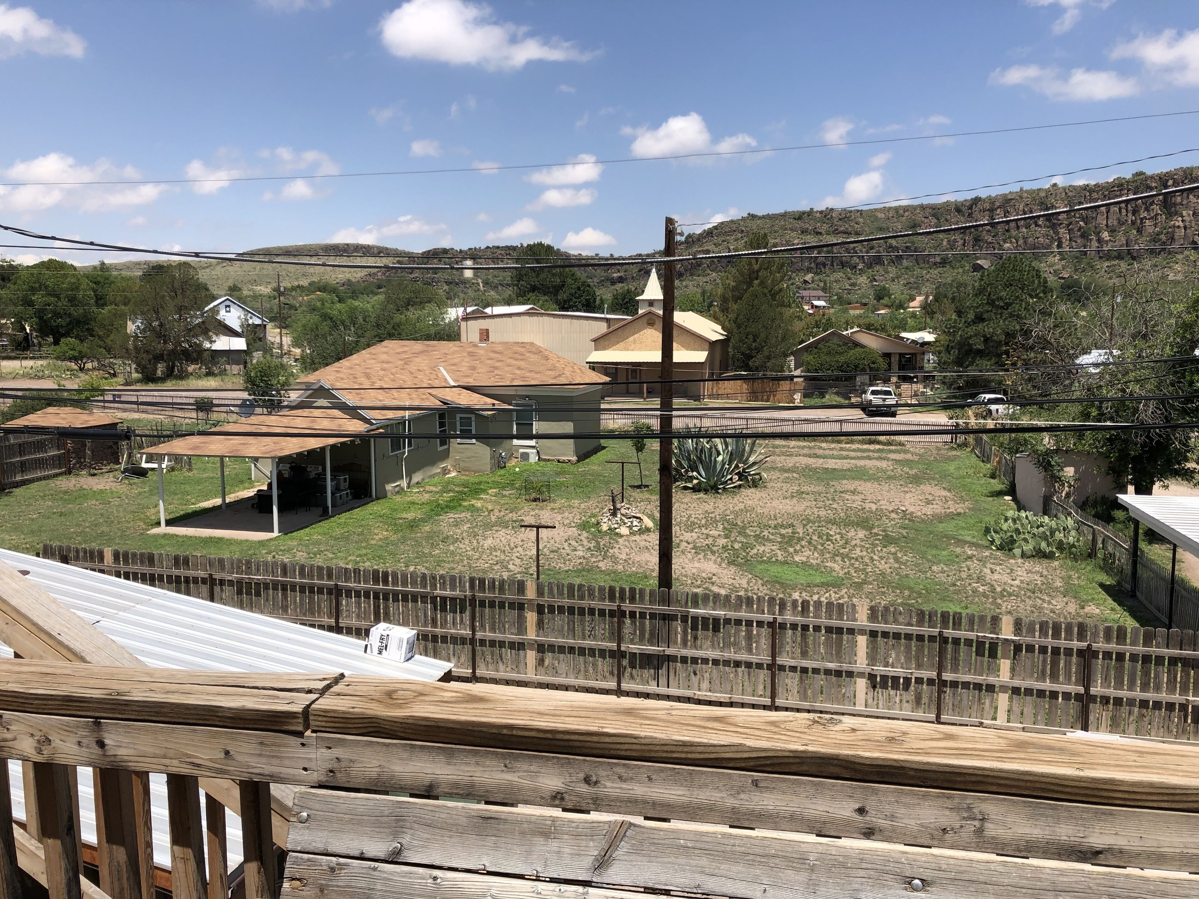A fenced property with a house, a covered area, and a hilly landscape in the background.