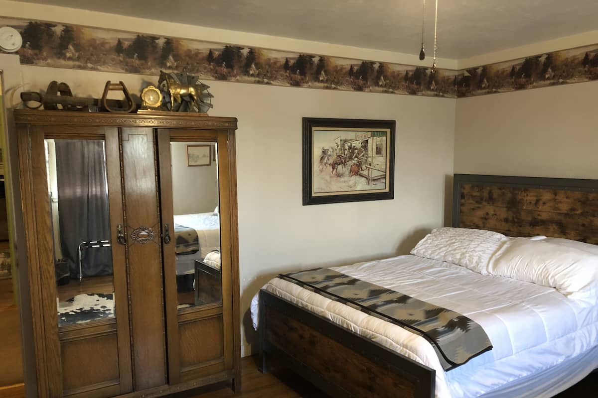 A bedroom with a wooden wardrobe, a bed with white bedding, a framed painting on the wall, and a wooden headboard.