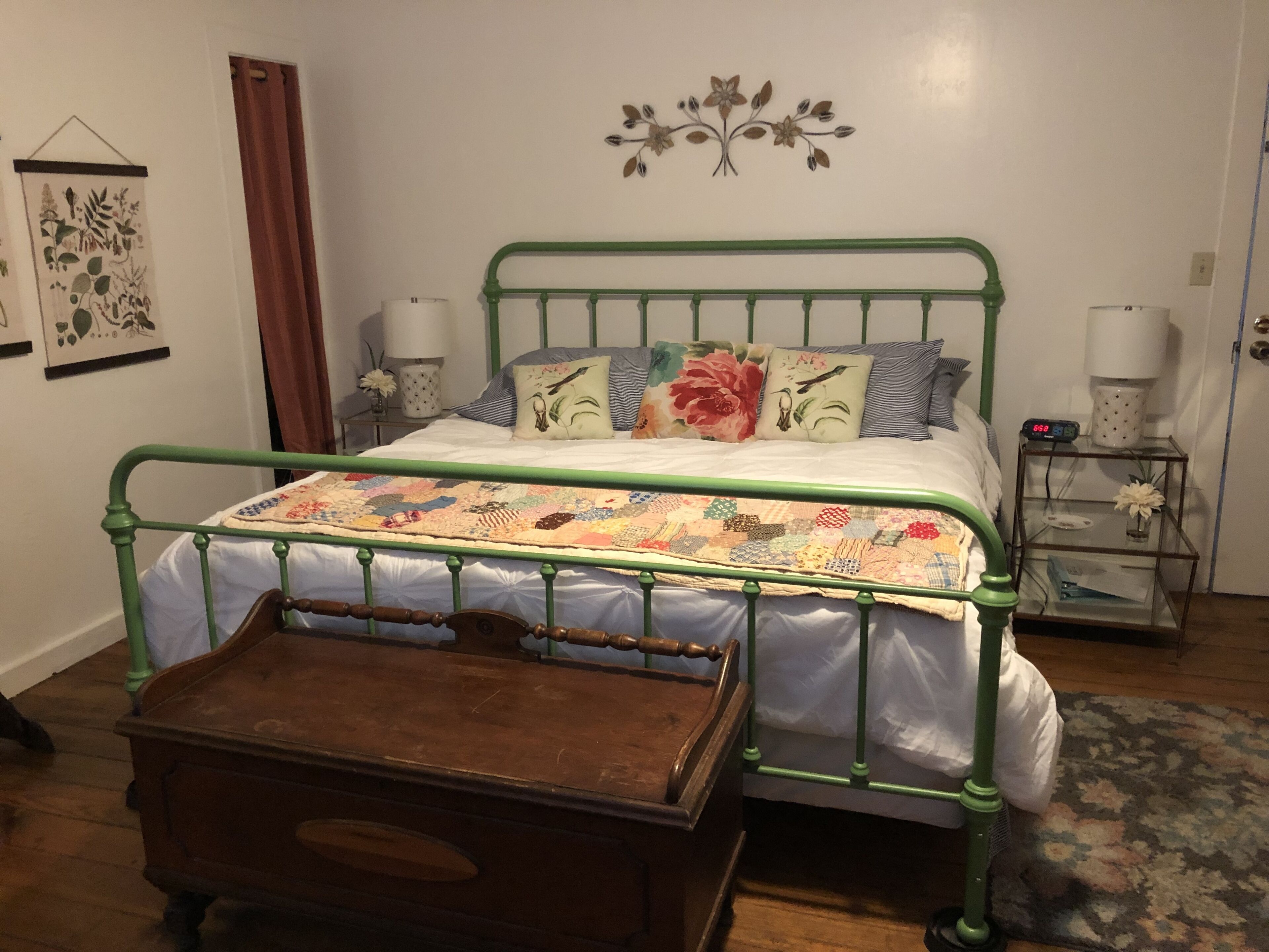 A bed with a green metal frame, a quilt, and multiple pillows. There is a wooden chest of drawers in front of the bed.