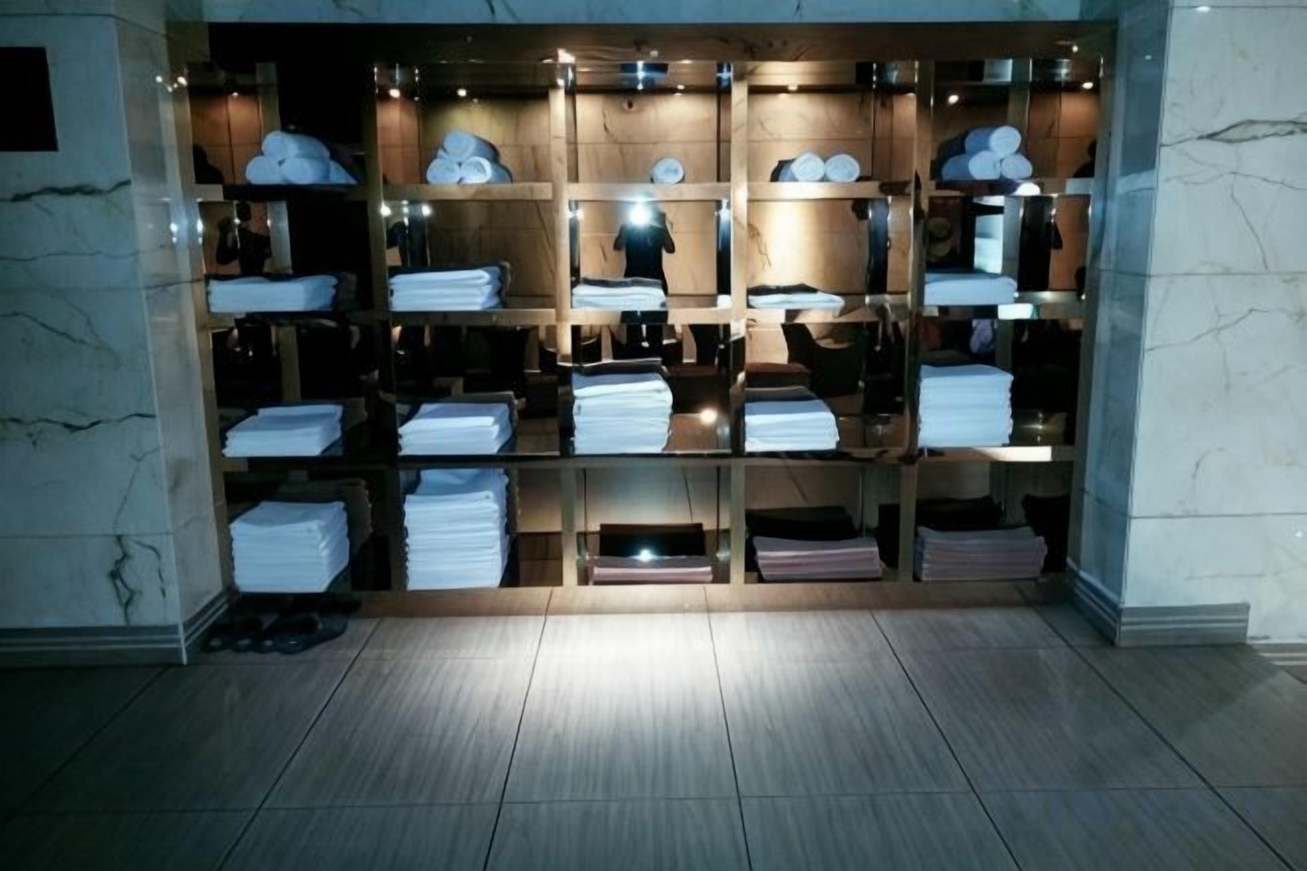 A hotel room with a wooden floor, a marble wall, and a built-in wardrobe with shelves and drawers.