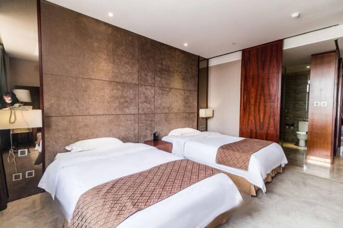 A hotel room with two beds, a large mirror, a wooden panel wall, and a bathroom visible through an open door.