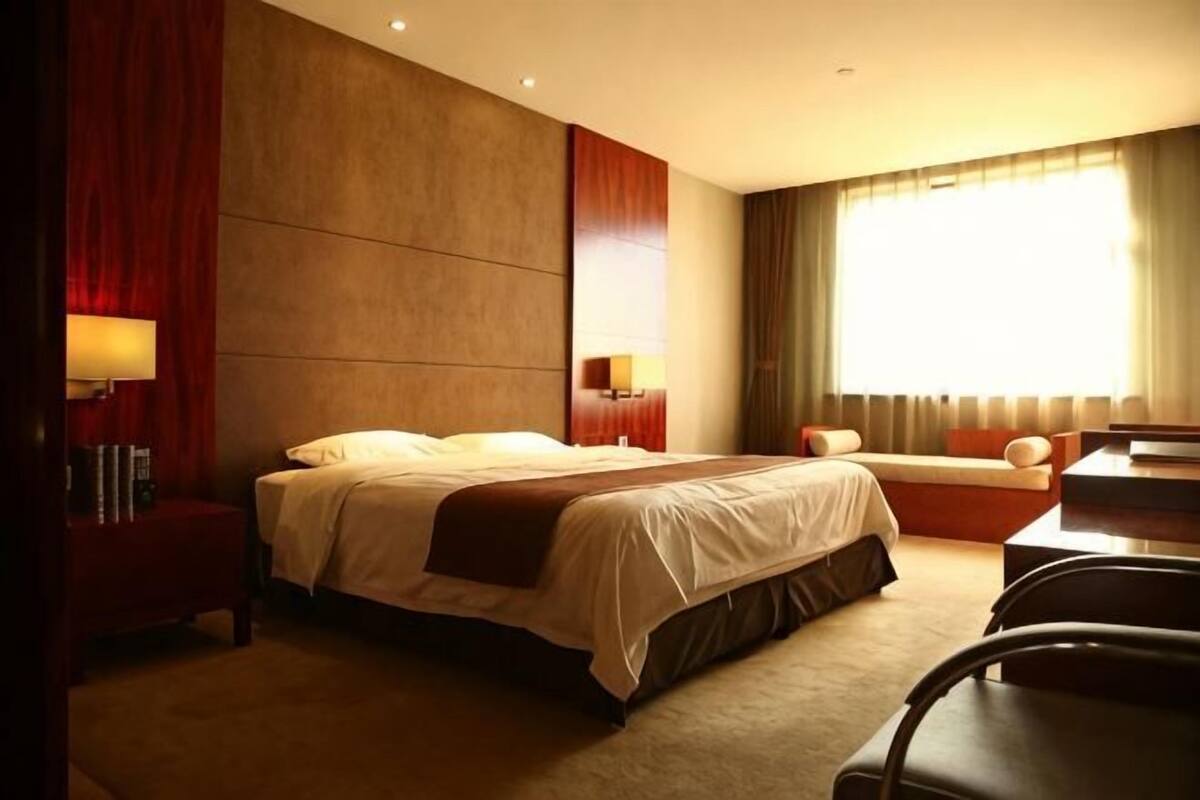 A hotel room with a large bed, bedside tables, a desk, and a window with curtains.