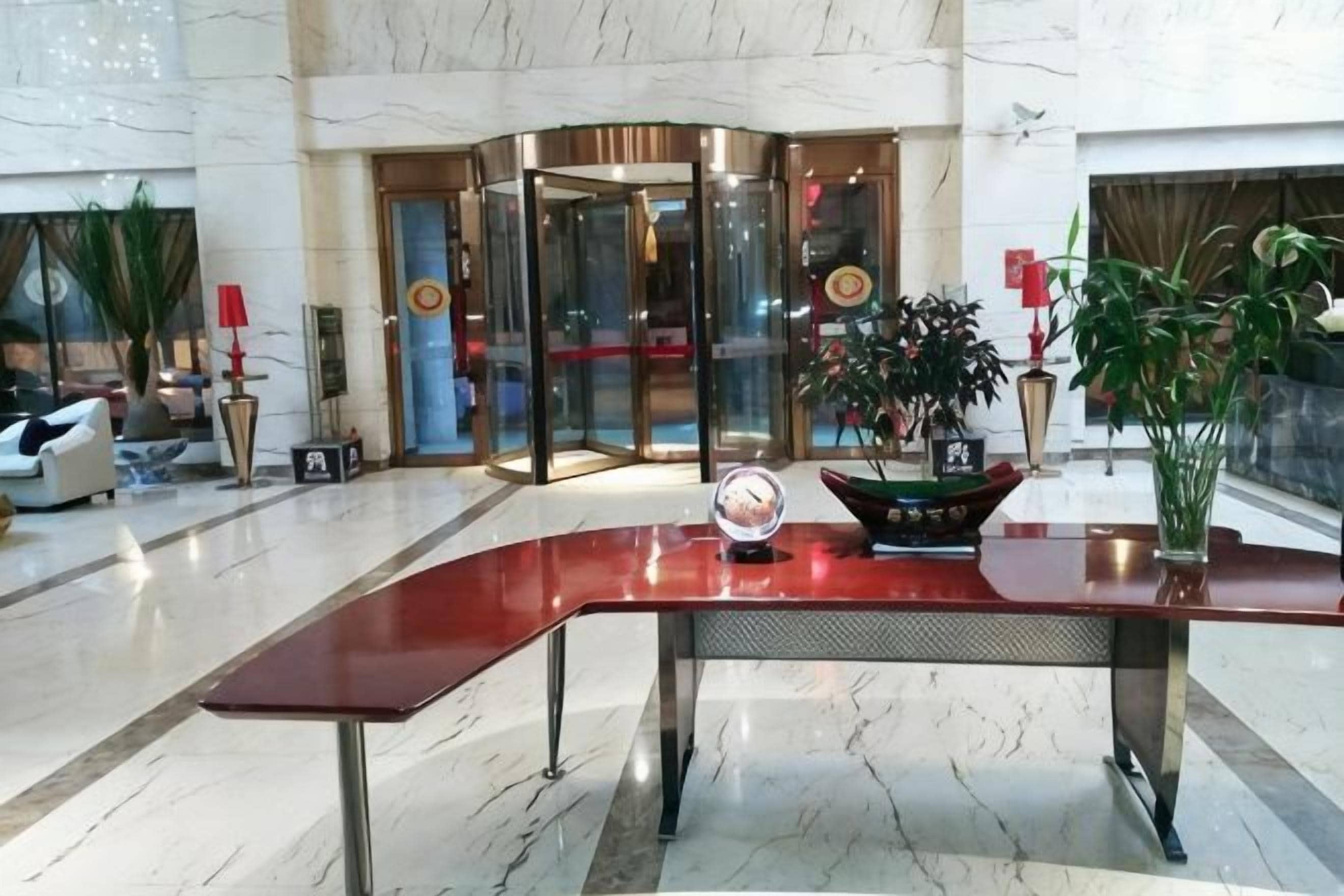 A lobby with a curved reception desk, a revolving door, and potted plants.