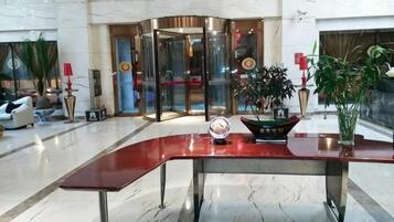A lobby with a curved reception desk, a revolving door, and potted plants.