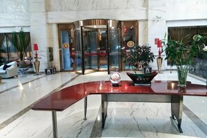 A lobby with a curved reception desk, a revolving door, and potted plants.