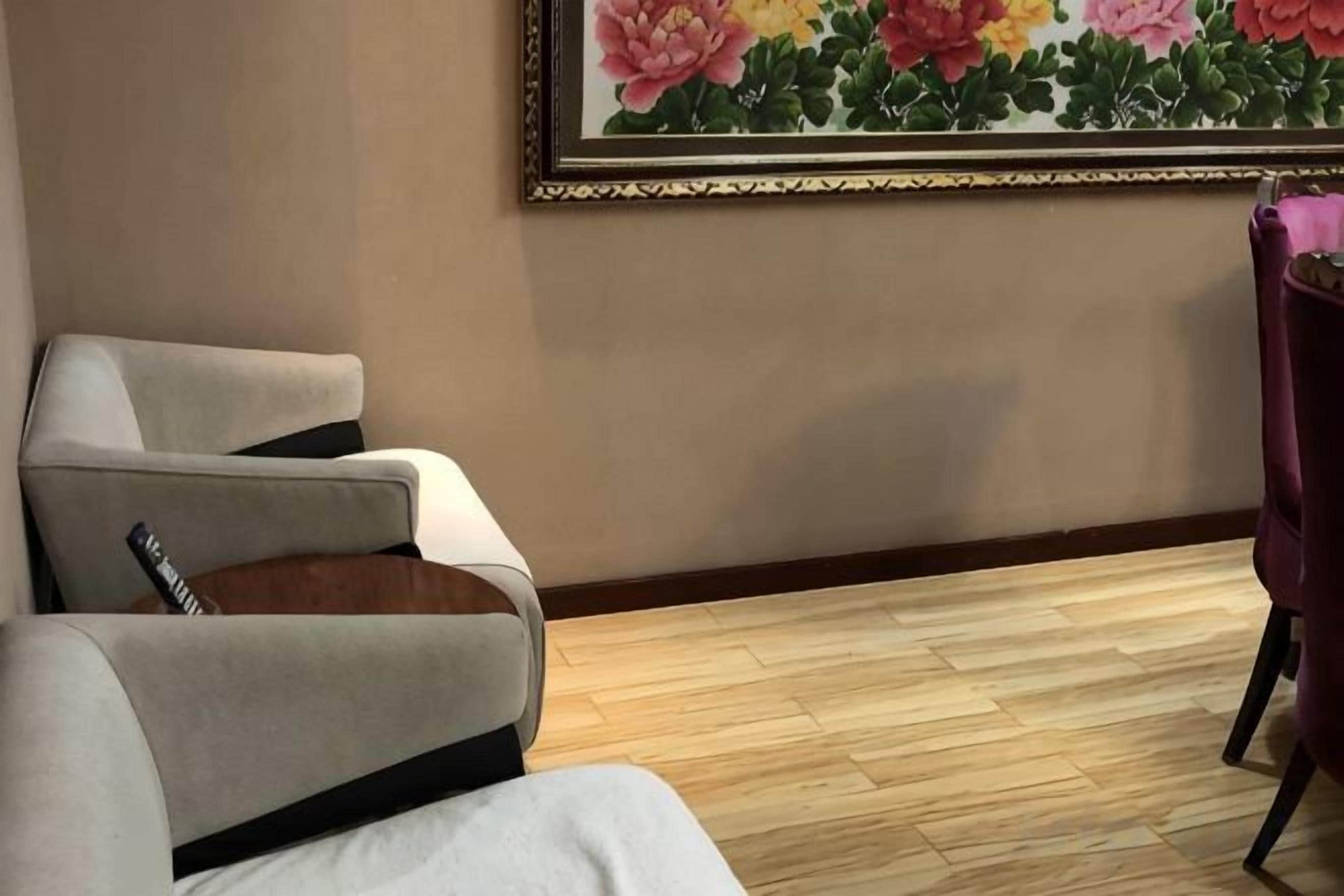 A hotel room with two armchairs, a wooden floor, and a framed floral artwork on the wall.