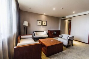Una habitación de hotel moderna con sofá, sillón y una mesa de centro de madera. Hay dos cuadros en la pared, una lámpara y un armario.