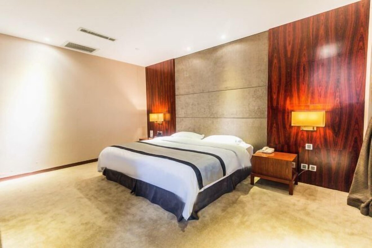 A hotel room with a bed, two bedside lamps, a nightstand, and a wall-mounted lamp.