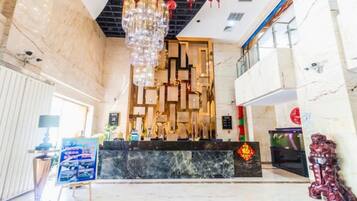 A hotel lobby with a reception desk, a chandelier, and a decorative wall.