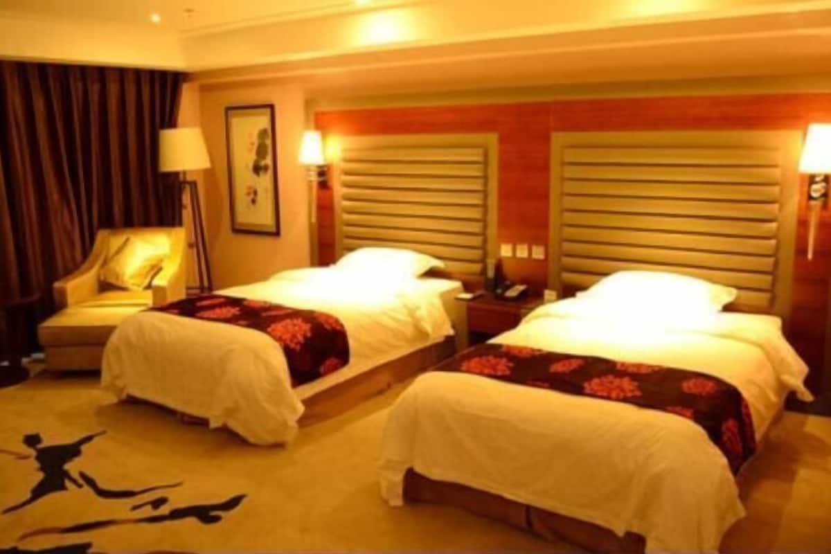 A hotel room with two beds, a sofa, a lamp, and a carpet with a runner.