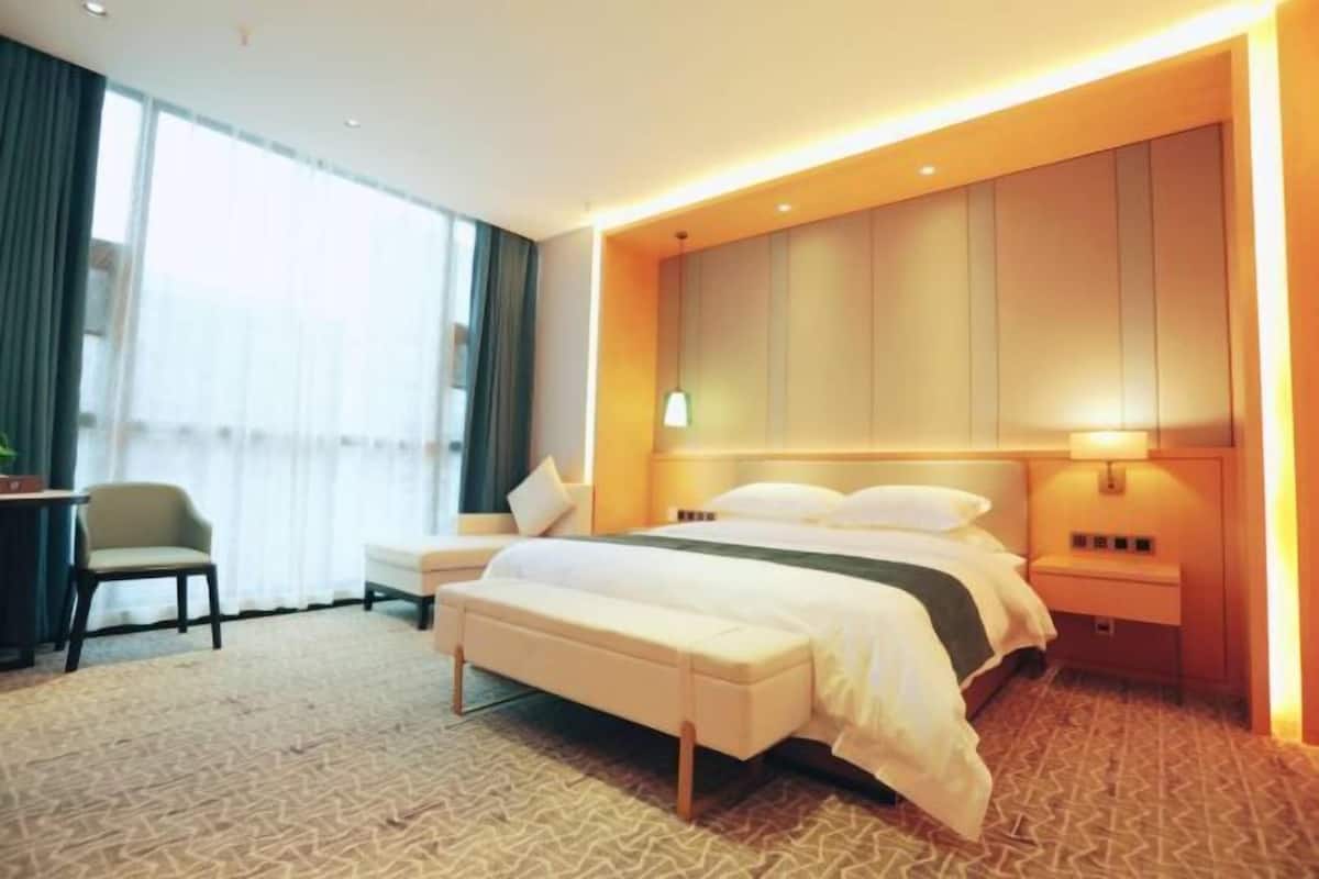 Habitación de hotel con cama, mesita de noche, banco y vistas al exterior.