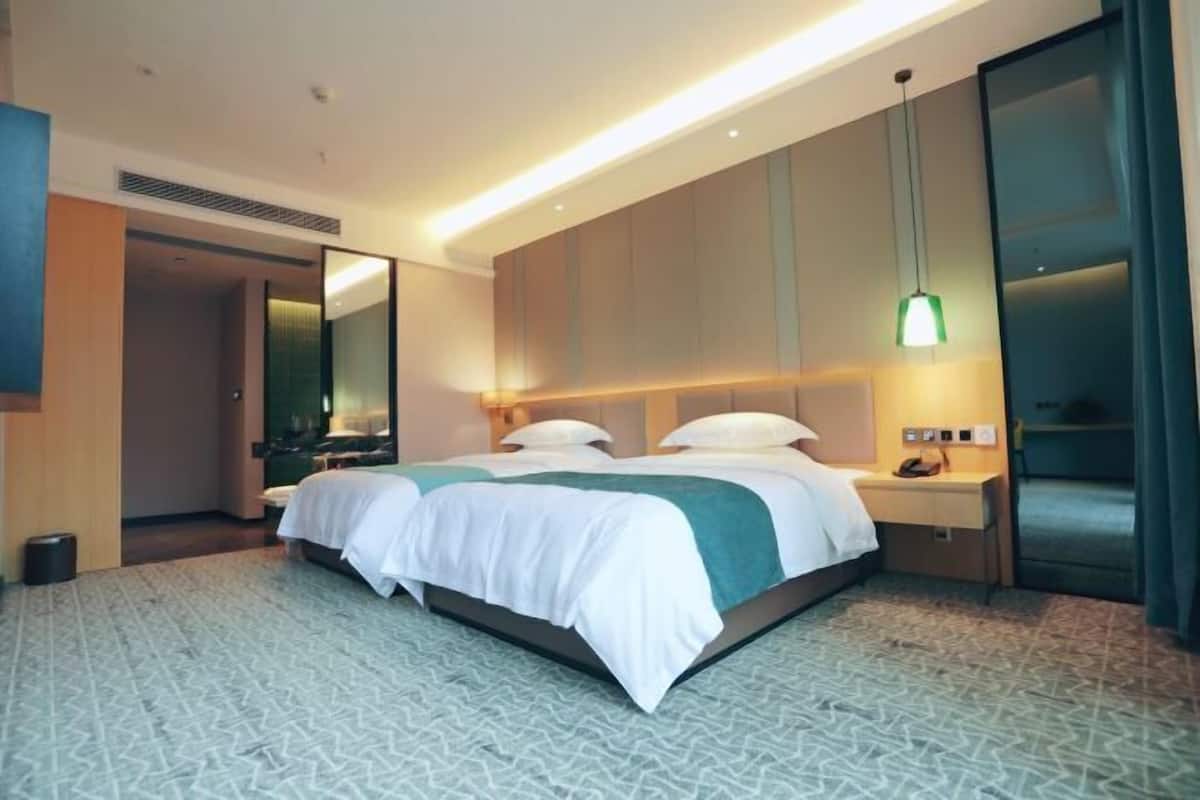 Una habitación de hotel moderna con una cama grande, una mesita de noche, un espejo y una lámpara de pared.