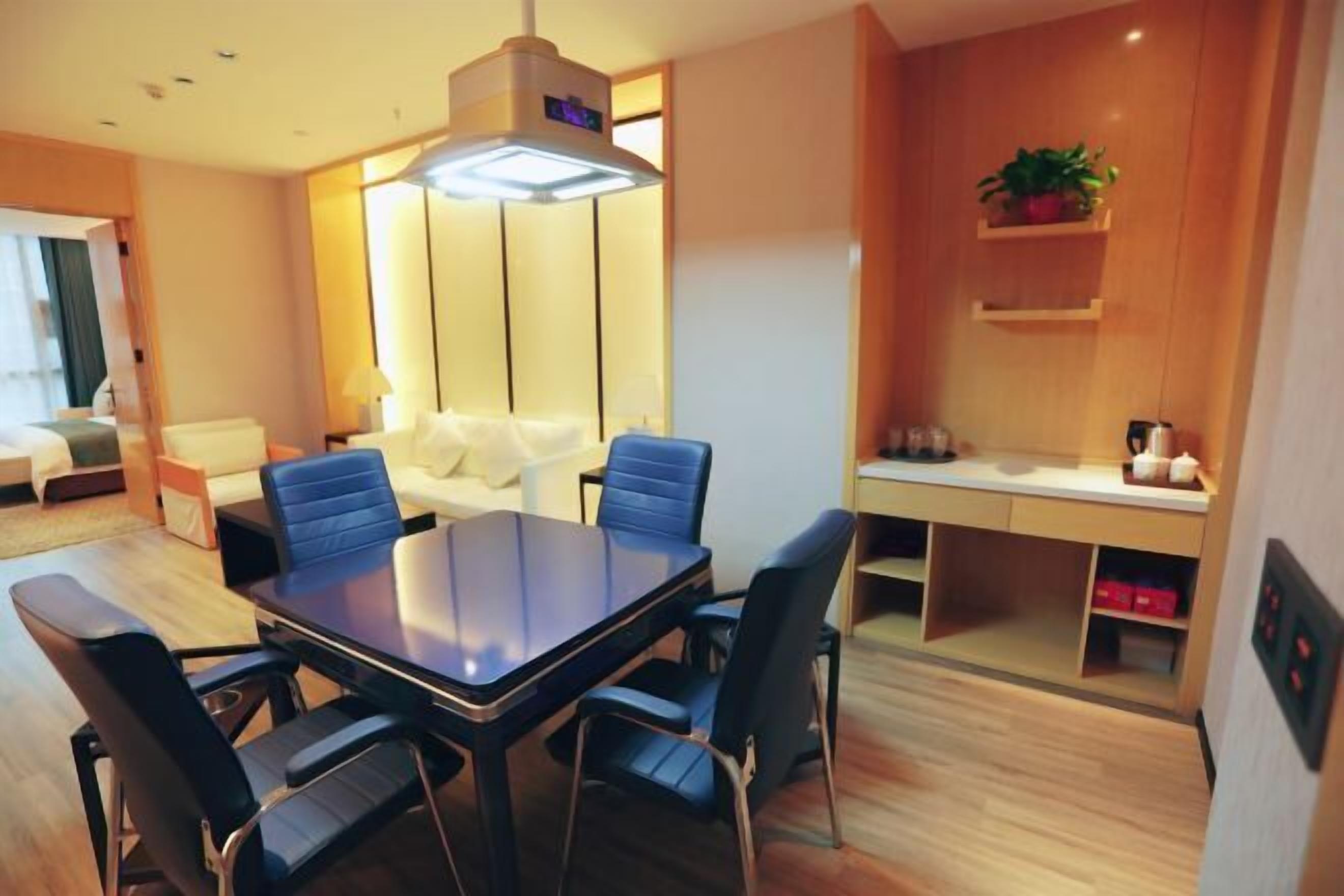 A modern hotel room with a dining table, chairs, a sofa, a desk, and a plant.