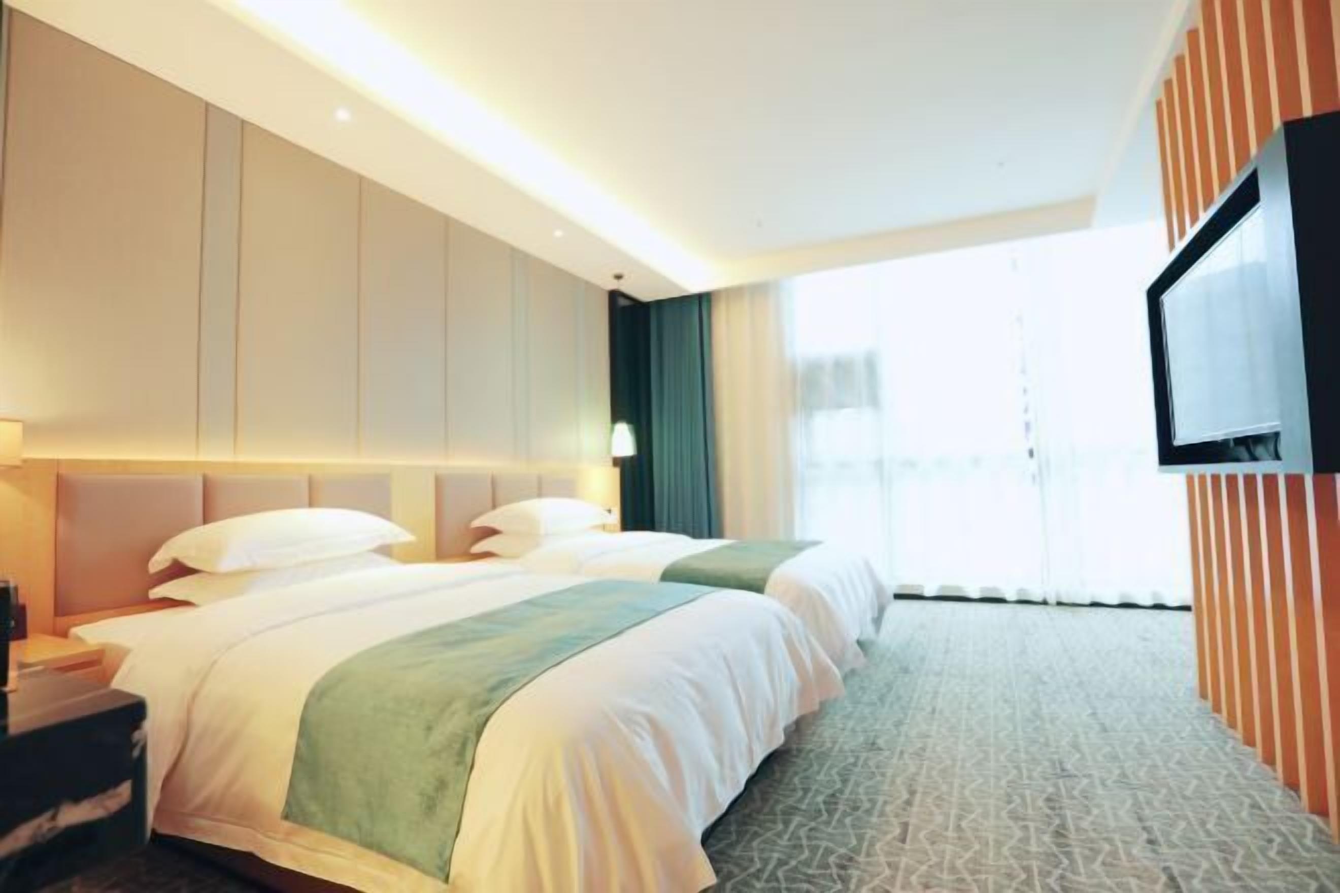 Une chambre d’hôtel avec deux lits, un téléviseur à écran plat fixé au mur et une grande fenêtre.