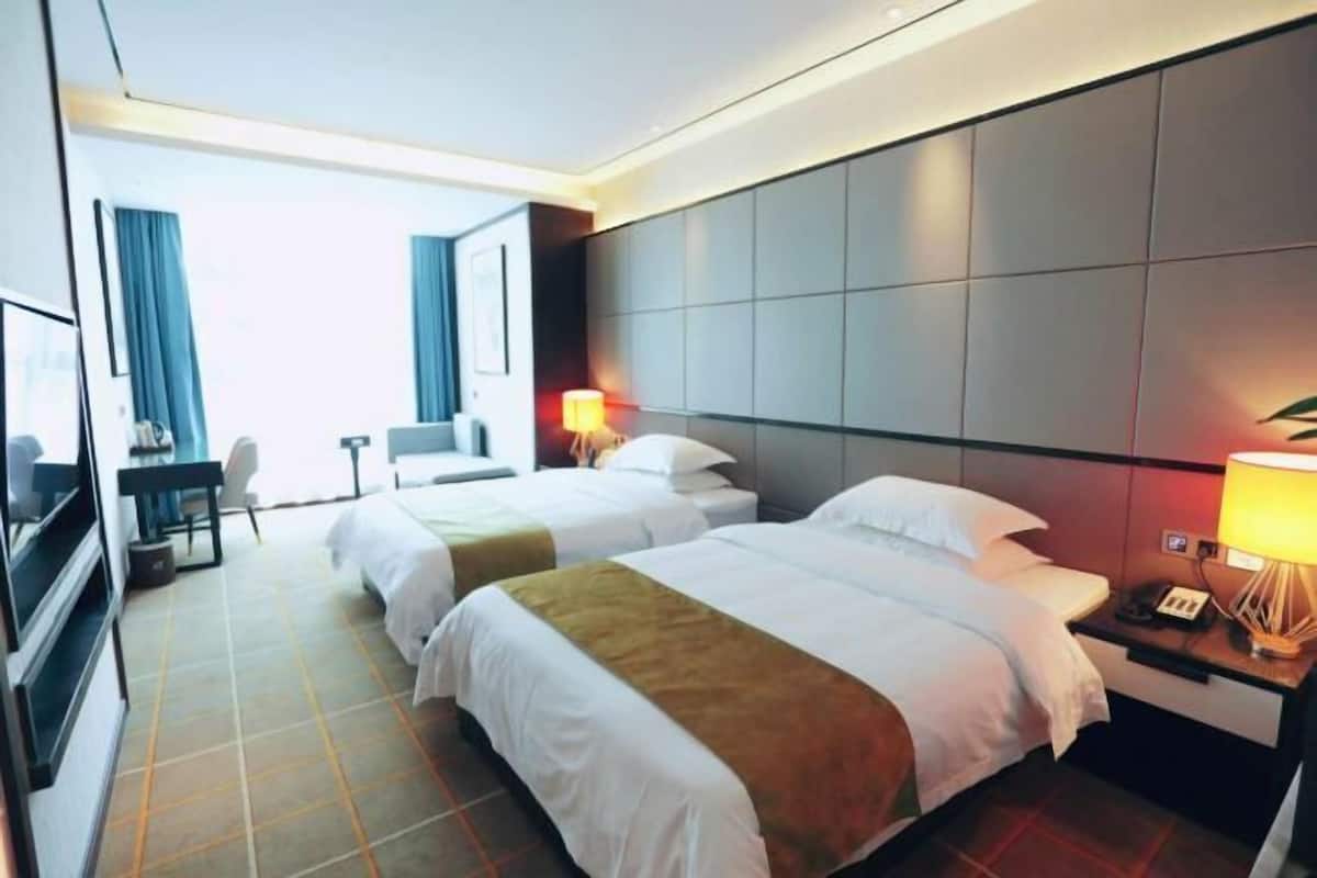 Habitación de hotel con dos camas, un escritorio, una silla y un televisor.