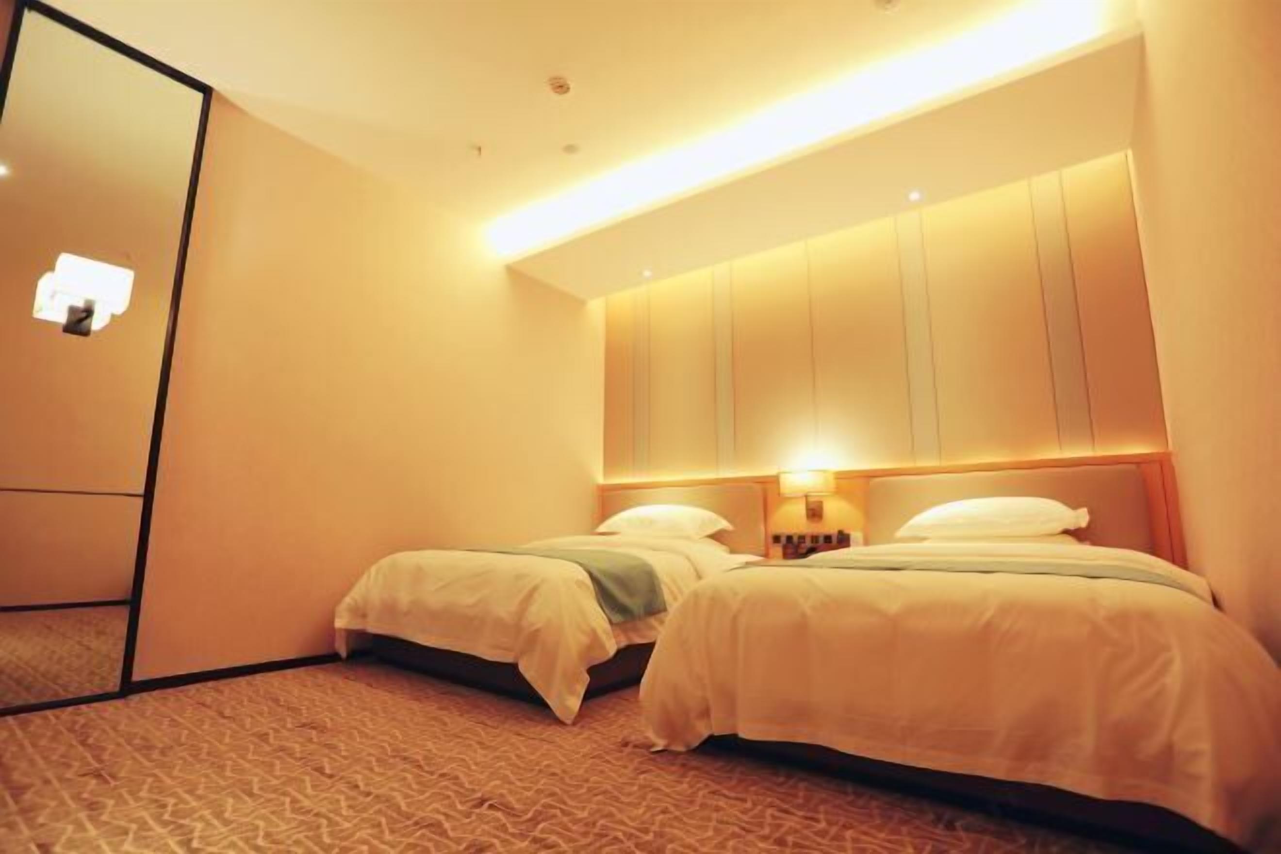 A hotel room with two beds, a large mirror, and a wall-mounted light fixture.