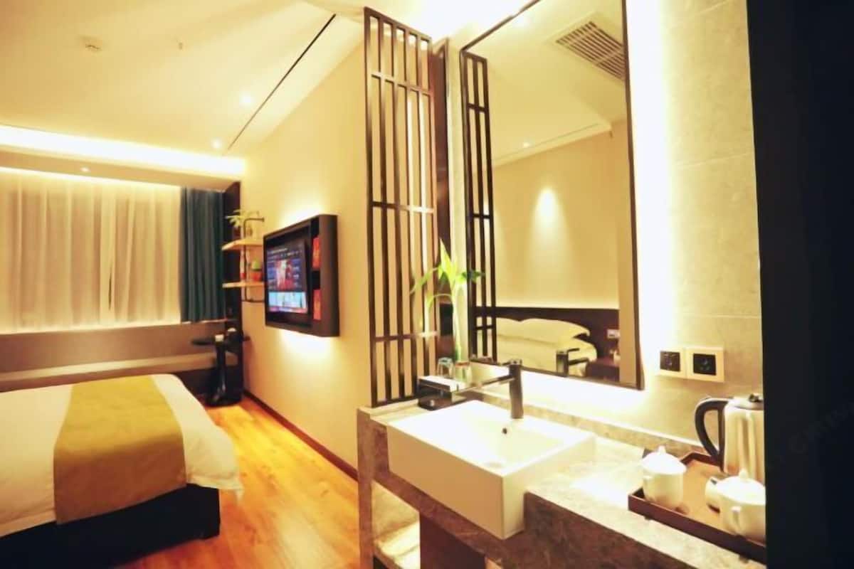 Habitación de hotel con cama, televisión, baño con lavamanos y espejo.