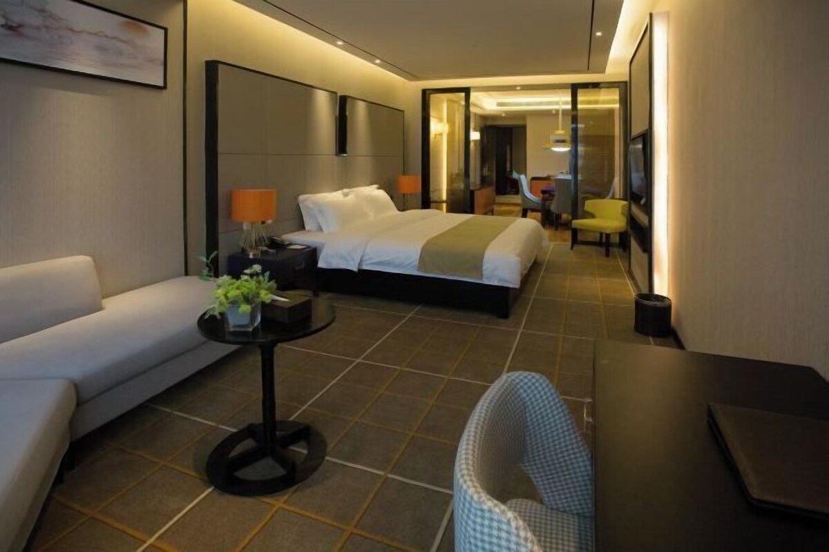 A modern hotel room with a bed, a sofa, a small table with a plant, a chair, and a desk.