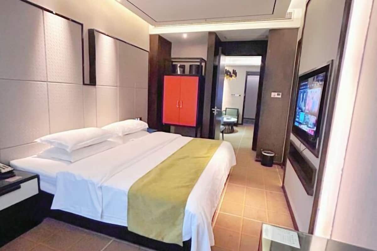 Habitación de hotel con cama, televisor, armario y baño visible a través de una puerta abierta.