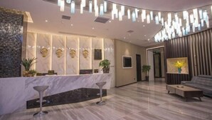 A modern reception area with a marble counter, two bar stools, a seating area with a sofa and coffee table, and decorative wall panels. - Laimei Hotel (Jianshi)