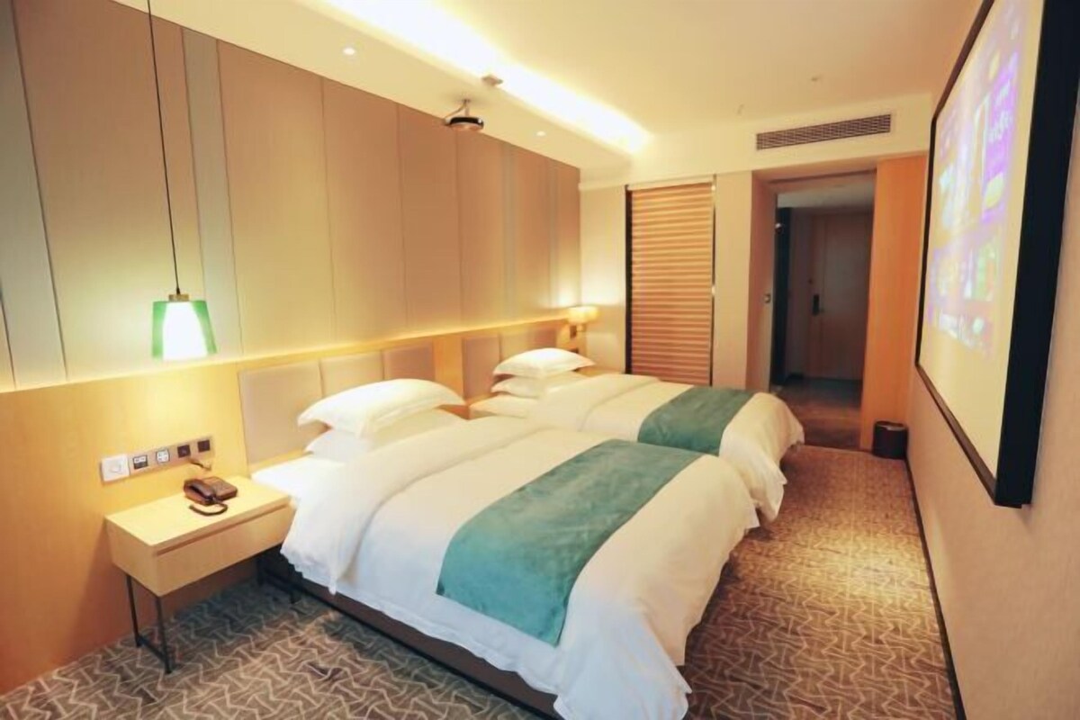 A hotel room with a bed, bedside table, lamp, and a wall-mounted television.