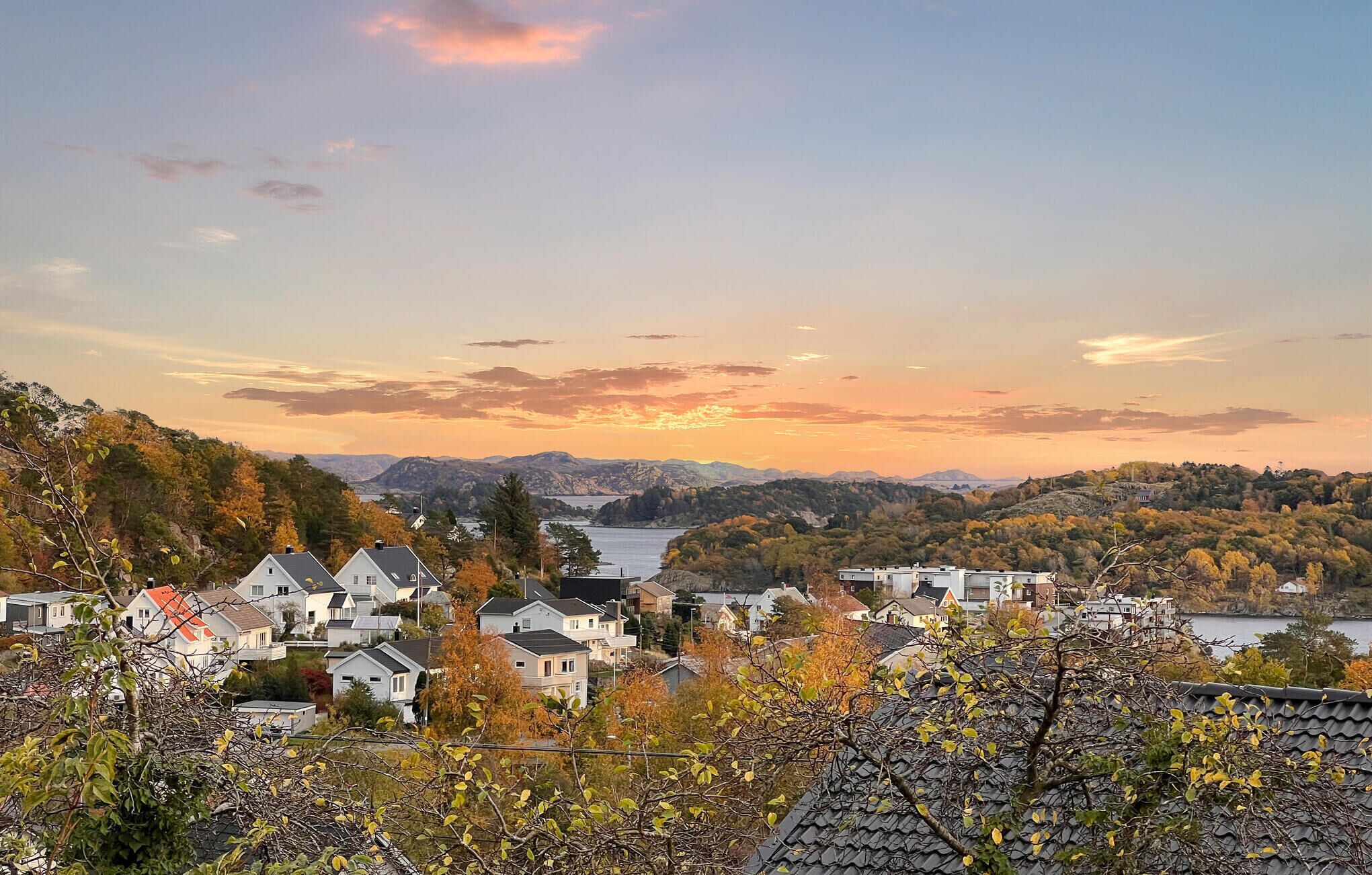 Un quartier résidentiel avec des maisons et un lac, entouré de collines et d’un paysage automnal aux couleurs flamboyantes.