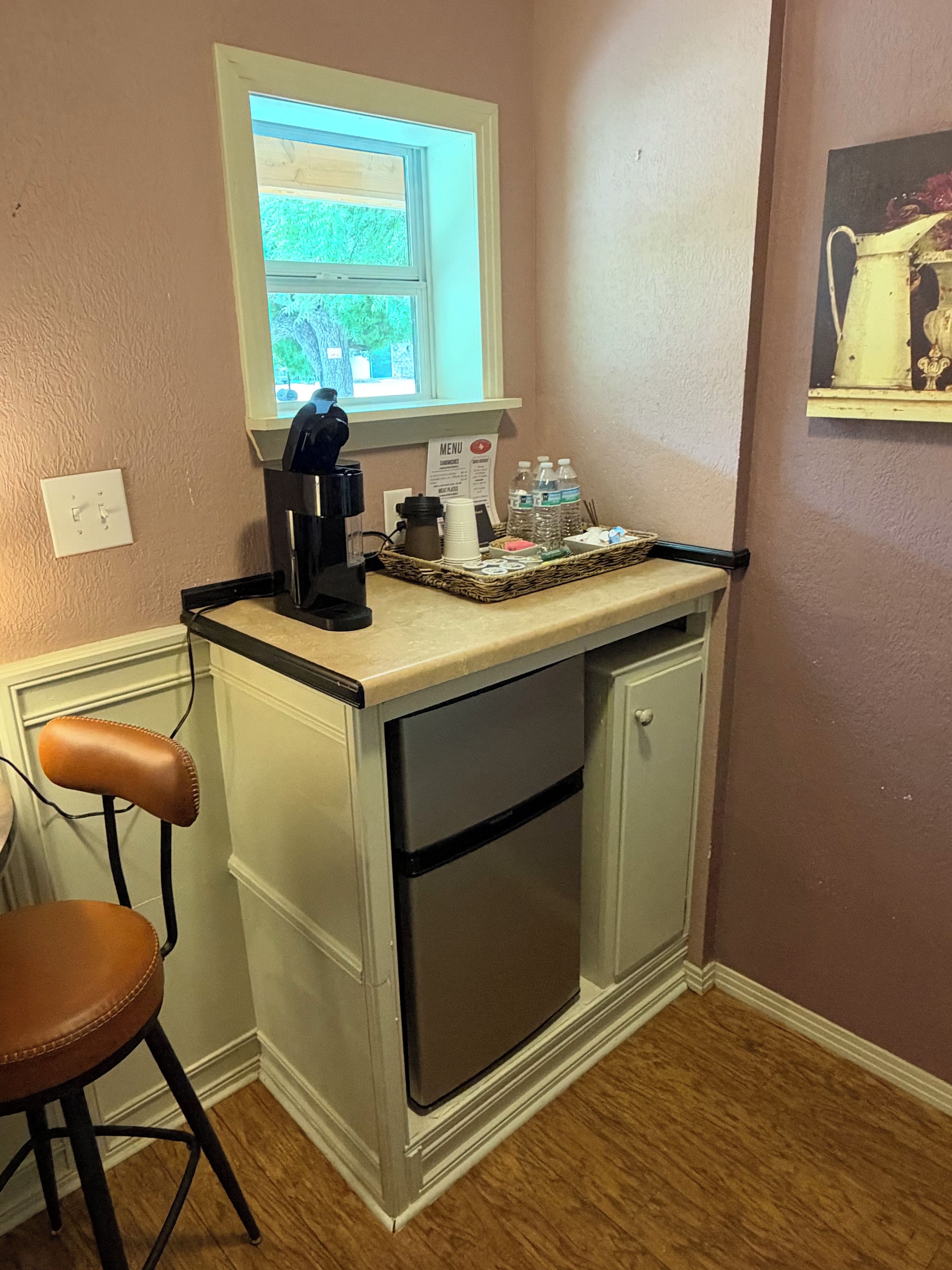 Una kitchenette compacta con cafetera, un refrigerador pequeño y una ventana con vista a follaje.